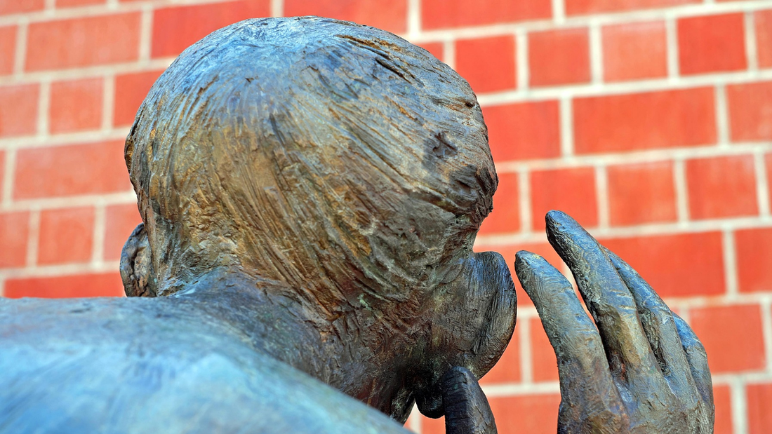he back of a statue's head with one hand cupped to an enlarged ear, symbolizing the art of listening for unique expressions and cultural language
