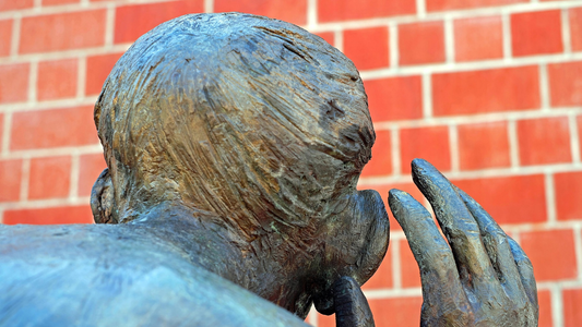 he back of a statue's head with one hand cupped to an enlarged ear, symbolizing the art of listening for unique expressions and cultural language